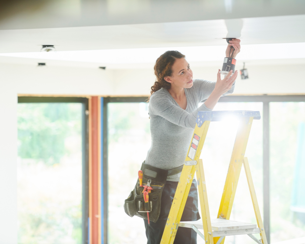 Electrician installing a recessed ceiling light in a residential or commercial space.